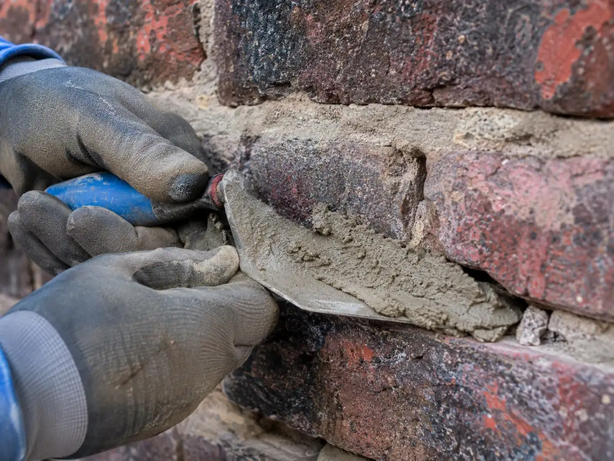 Fresh mortar being worked into a repointed joint on a chimney with a trowel